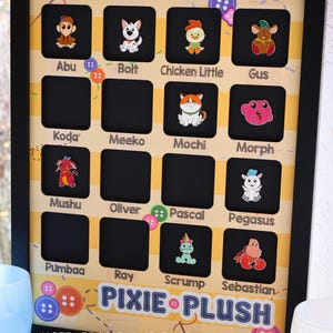 May include: Black framed display board with character pins. The board has a yellow background with character names like "Abu", "Bolt", "Chicken Little", and "Gus". The text "PIXIE PLUSH" is displayed at the bottom. The text "NOTE: FRAME AND PINS NOT INCLUDED" is also visible.