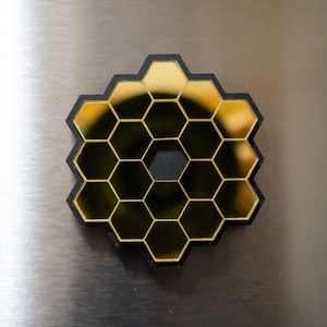 May include: A black and gold honeycomb-shaped object with a reflective surface. The object is made of multiple hexagonal pieces.
