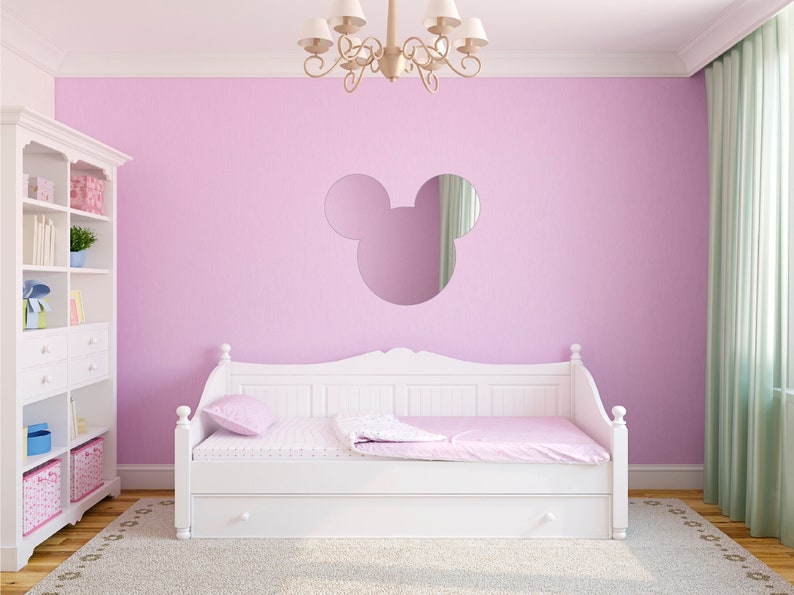 K&ouml;nnte beinhalten: Ein wei&szlig;es Tagesbett mit einer rosa Bettdecke und einer rosa Wand dahinter. Ein Mickey-Mouse-f&ouml;rmiger Spiegel h&auml;ngt an der Wand &uuml;ber dem Tagesbett.