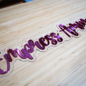 May include: Pink acrylic sign with the text "Empress Arrow" in a cursive font.