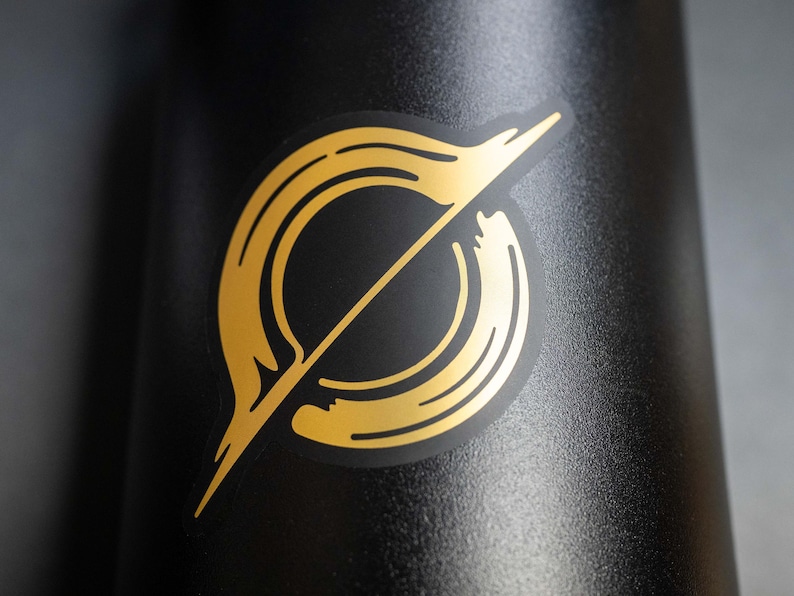 May include: A gold sticker with a stylized circle design on a black background.