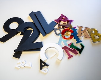 May include: Assortment of colorful, mirrored letters and black and white numbers. The letters are in various colors, including red, pink, blue, green, gold, and silver. The numbers are in black and white.