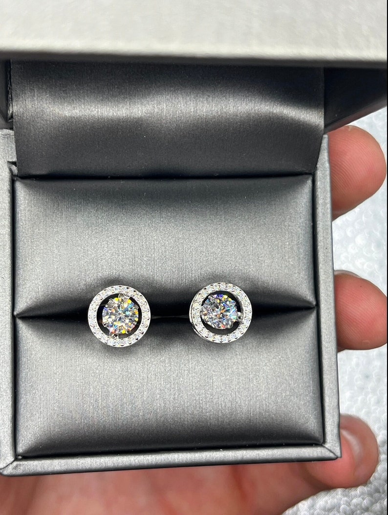 May include: A pair of silver stud earrings with a round, clear stone surrounded by a halo of smaller stones.