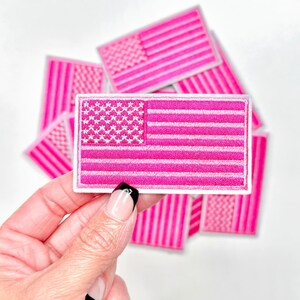 May include: A stack of pink felt American flag patches with white stitching. The patches are approximately 3 inches by 5 inches.