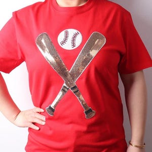 May include: Red t-shirt with a gold sequin baseball bat and ball design.