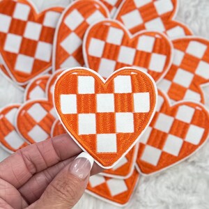 Peut inclure: Un tas de patchs en forme de cœur à carreaux orange et blancs. Les patchs sont en feutre et ont un contour blanc.