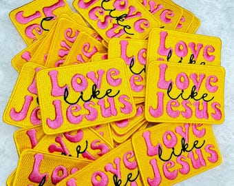 Op de afbeelding: Een stapel gele stoffen patches met roze letters die "Love like Jesus" zeggen.