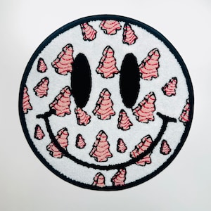 May include: A white smiley face rug with a black outline and pink and red tree-shaped designs. The rug is round and has a fuzzy texture.