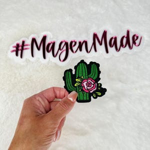 May include: A green cactus with a pink flower embroidered patch. The patch has the text "#MagenMade" in pink lettering.