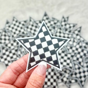 Peut inclure: Un gros plan sur un patch en forme d'étoile à carreaux noirs et blancs. Le patch est tenu dans une main et il y a plusieurs autres patchs similaires en arrière-plan.
