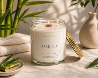 Op de afbeelding: Een glazen potkaars met een houten lont en een gouden deksel. Het etiket luidt "EVES & CO BAMBOO" met afmetingen van 221 g en 40 uur. De kaars staat naast een klein keramisch schaaltje met bamboe.