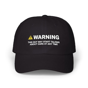 Puede incluir: Una gorra de béisbol negra con un icono de triángulo de advertencia amarillo y texto blanco que dice: WARNING THIS GUY MAY START TALKING ABOUT CARS AT ANY TIME. La gorra tiene una visera curva y una corona estructurada con un botón central.