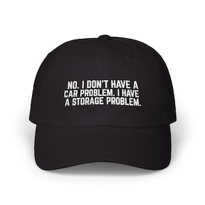 Puede incluir: Una gorra de béisbol negra con texto bordado en blanco en la parte frontal que dice: NO. I DON'T HAVE A CAR PROBLEM. I HAVE A STORAGE PROBLEM. La gorra tiene una corona estructurada, una visera curva y un botón en la parte superior central.