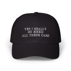 Puede incluir: Una gorra de béisbol negra con texto bordado en blanco en la parte frontal que dice: YES I REALLY DO NEED ALL THESE CARS. La gorra tiene una corona estructurada, una visera curva y un botón en la parte superior, con un diseño sencillo.