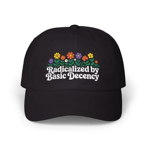May include: A black baseball cap featuring an embroidered design of colourful flowers in shades of yellow, orange, red, and purple with green stems. Below the floral arrangement, the text reads "Radicalized by Basic Decency" in white.