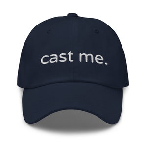 May include: A navy blue baseball cap with white embroidered text that reads "cast me."