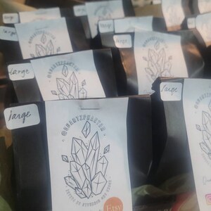 May include: A close-up of several black boxes with white labels. The labels have a logo of a crystal cluster and the text "QuartzPhantom" and "Etsy". The boxes are labeled "large".