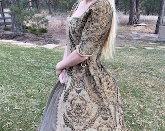 May include: A long, green and gold brocade dress with a lace trim. The dress has a fitted bodice and a full skirt.