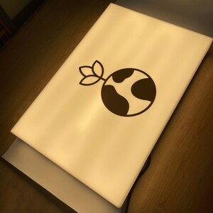 May include: A white light box with a black and white logo of a globe with a sprout growing from the top. The logo is on a white background.