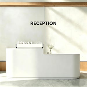 May include: A contemporary white reception desk with the word "RECEPTION" in black above. The desk features a curved design and a small countertop with a coffee machine and glassware. A vase of flowers is on the countertop.