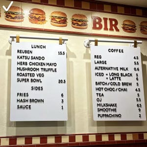Op de afbeelding: Twee witte menuborden met zwarte tekst met lunch- en koffie-opties. Het lunchmenu bevat items als Reuben en Mushroom Truffle. Het koffiemenu biedt opties als Latte en Smoothie. Boven de borden staan afbeeldingen van hamburgers.