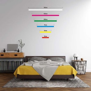 K&ouml;nnte beinhalten: Eine wei&szlig;e Wand mit f&uuml;nf horizontalen Linien in verschiedenen Farben und L&auml;ngen. Die Linien sind mit ihren L&auml;ngen in Zentimetern beschriftet: 150 cm, 120 cm, 100 cm, 75 cm, 50 cm und 30 cm. Die Linien sind wei&szlig;, rosa, gr&uuml;n, blau, gelb und rot.