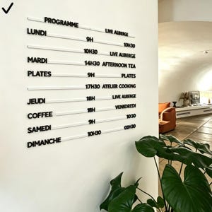 May include: A white wall displays a black and white schedule. The word "PROGRAMME" is at the top, with days of the week and times listed below. The schedule includes events like "LIVE AUBERGE" and "AFTERNOON TEA".