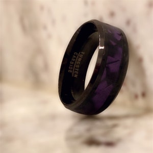 Pode incluir: Um anel de carboneto de tungst&ecirc;nio preto com uma incrusta&ccedil;&atilde;o roxa. O anel tem as palavras "TUNGSTEN CARBIDE" gravadas na lateral.