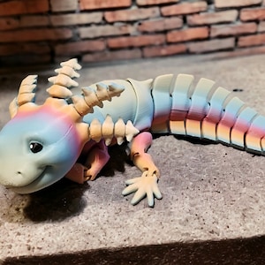 May include: A colorful, segmented, articulated toy axolotl with a smiling face and large eyes. The toy is painted in shades of blue, pink, and yellow.