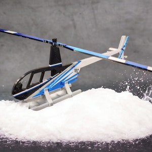 May include: A blue and white toy helicopter with black accents is landing in a pile of white powder. The helicopter has a clear cockpit and a spinning rotor.