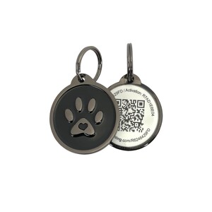May include: Two black pet ID tags. One tag features a paw print with a heart in the center. The other tag has a QR code and the text "29FD / Activation: R7AD1E6E04". The tags are round with a metal loop.