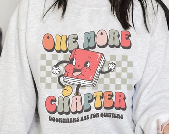 May include: A gray sweatshirt with a colorful graphic of a book character saying "One More Chapter" and "Bookmarks are for quitters".