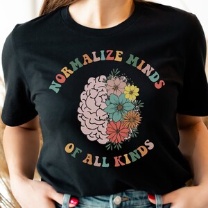 May include: A black t-shirt featuring a graphic of a brain with flowers and the text "Normalize Minds of All Kinds" in rainbow colours.