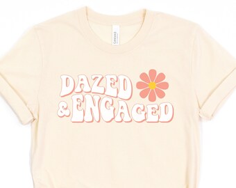 May include: A cream-coloured t-shirt with the text "Dazed & Engaged" in a retro font with a pink flower graphic.