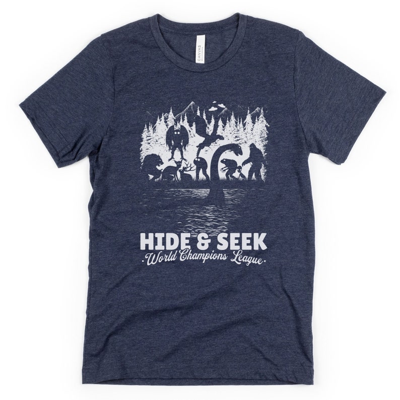 May include: A navy blue t-shirt with a white graphic of a group of mythical creatures playing hide and seek in a forest. The text "Hide & Seek World Champions League" is printed below the graphic.