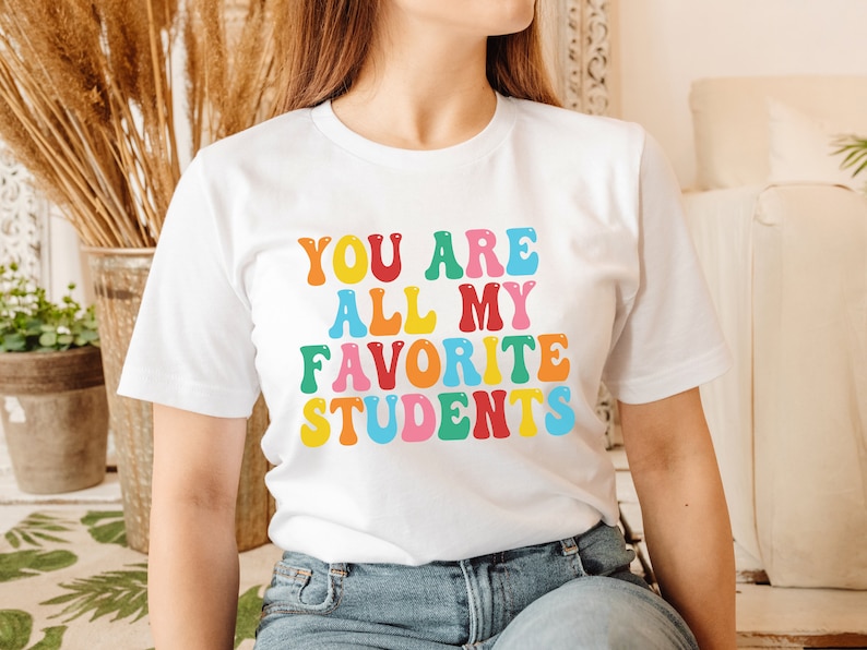 May include: White t-shirt with the text "You are all my favourite students" in colourful, outlined letters.