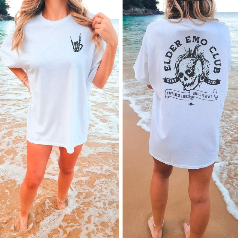 May include: White oversized t-shirt with a black skeleton hand making a rock and roll sign on the front and a black skull with flames on the back. The back of the shirt also has the text "Elder Emo Club" with the words "Stay Sad" above the skull and "Happiness Fades Emo Is Forever" below the skull.