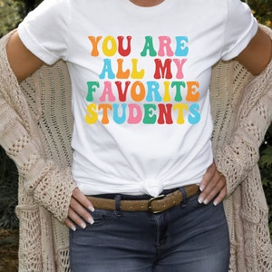 May include: White t-shirt with the text "You are all my favourite students" in colourful, retro-style lettering.