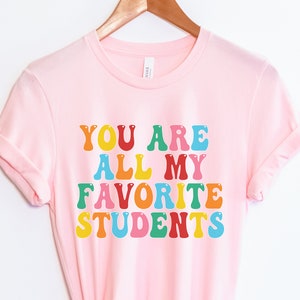 May include: Pink t-shirt with the text "You are all my favourite students" in rainbow colours.