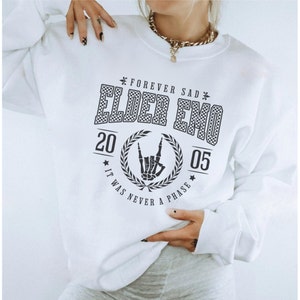 以下が含まれることがあります： 「Forever Sad* Elder Emo* 20 05 It Was Never A Phase*」と黒で書かれたグラフィックプリントが施された白いスウェットシャツ