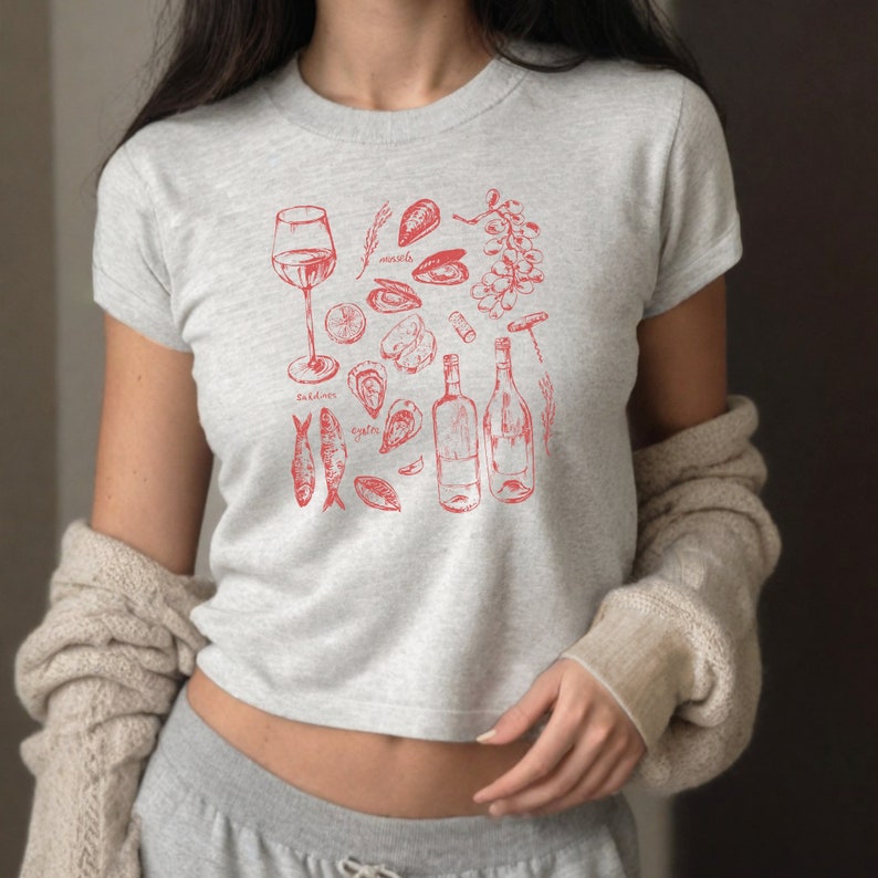 May include: A grey cropped t-shirt with a red illustration of wine, oysters, mussels, and sardines. The text "oysters", "mussels", and "sardines" is included in the design.