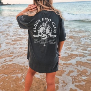 May include: A dark gray oversized t-shirt with a white graphic print of a skull with flames and the text "Elder Emo Club" with the text "Stay Sad" and "Happiness Fades Emo Is Forever" on a banner.