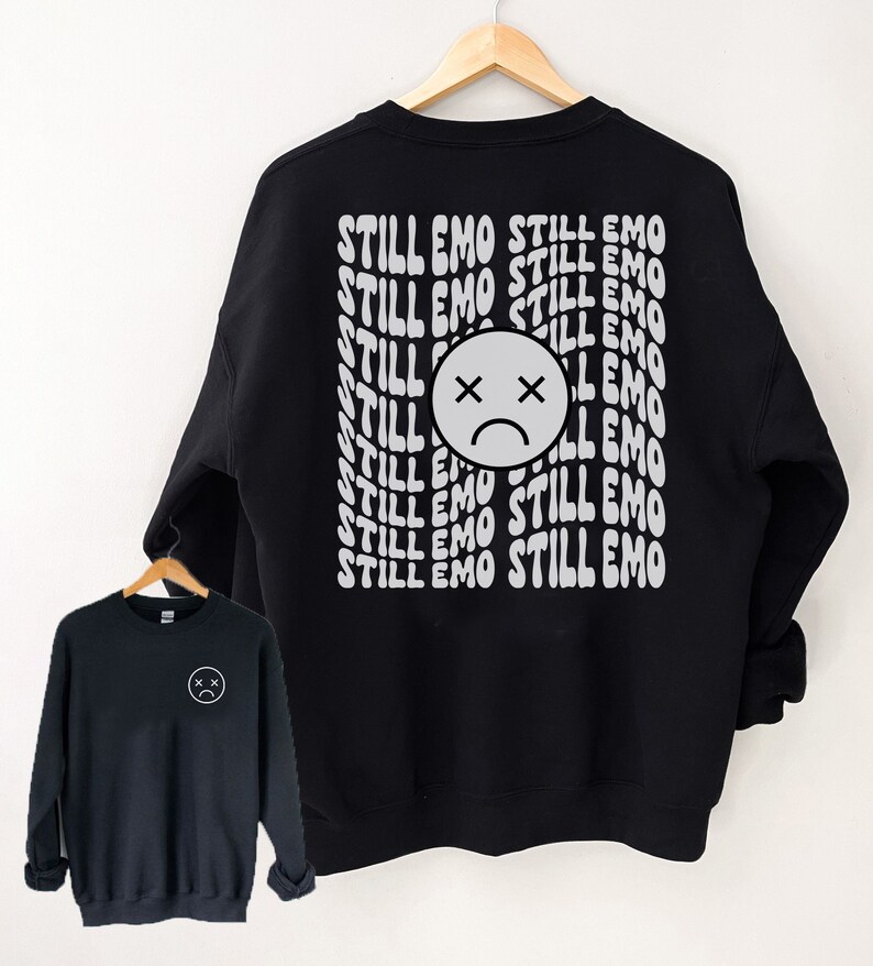 May include: Black sweatshirt with a white graphic print of a sad face and the text "STILL EMO" repeated multiple times.