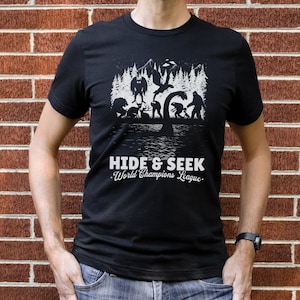 May include: Black t-shirt with a white graphic of various mythical creatures playing hide and seek in a forest. The text "Hide & Seek. World Champions League." is printed below the graphic.