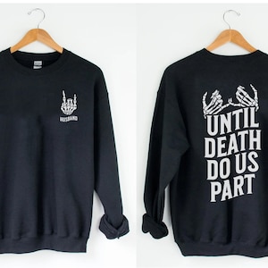 May include: Black sweatshirt with a skeleton hand making a rock and roll sign and the word "Husband" on the front. The back of the sweatshirt has a skeleton hand holding another skeleton hand with the text "Until Death Do Us Part".