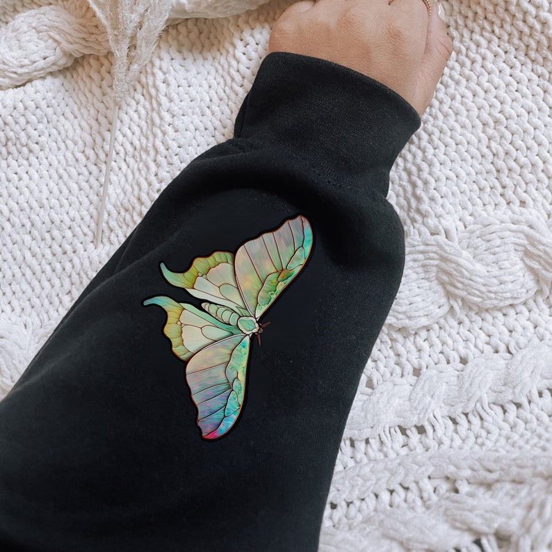 May include: Black sweatshirt with a colorful butterfly graphic print. The butterfly has iridescent wings with shades of green, blue, and purple.