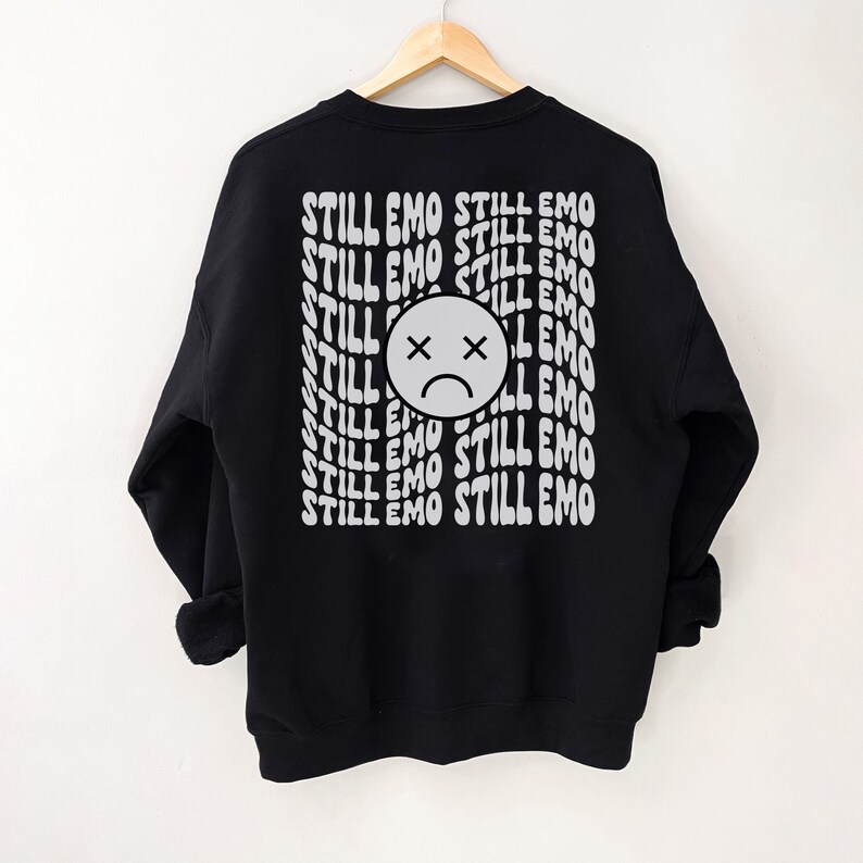 May include: Black sweatshirt with a white graphic print of a sad face and the text "STILL EMO" repeated multiple times.