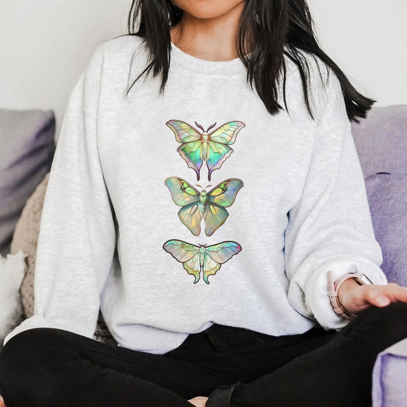 May include: A light gray sweatshirt with a design of three iridescent butterflies in a vertical row. The butterflies are green, blue, and yellow.