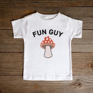 May include: White t-shirt with a black mushroom graphic and the text "FUN GUY" printed on the front.