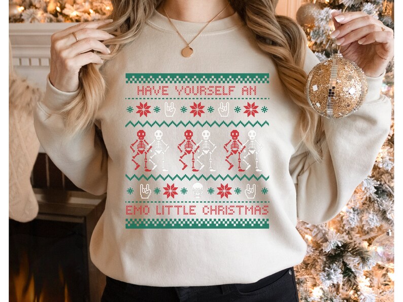 K&ouml;nnte beinhalten: Ein cremefarbener Pullover mit einem festlichen Design mit Skeletten in Rot und Wei&szlig;, Schneeflocken und dem Text "Have Yourself an Emo Little Christmas".